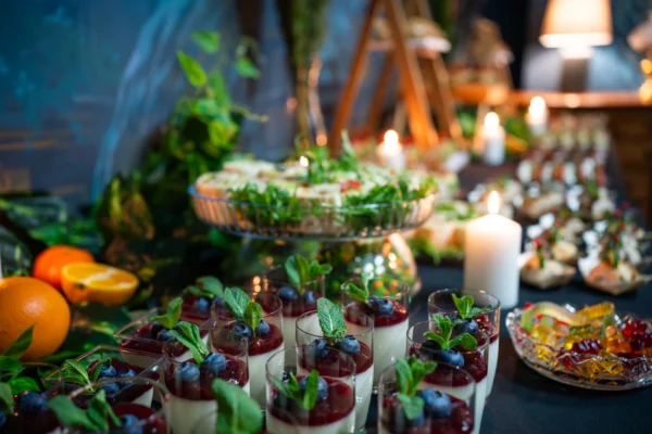 Desery panna cotta z owocami i miętą, podane na bufecie z dekoracjami i świecami.