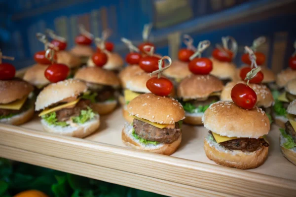Mini burgery z pomidorkiem koktajlowym na wykałaczce, serwowane dla dzieci.