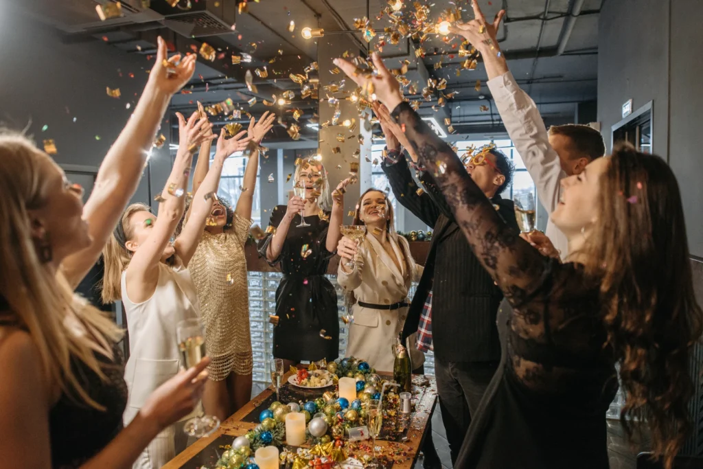 Grupa uśmiechniętych osób świętujących przy udekorowanym stole – toast, konfetti i entuzjazm tworzą atmosferę udanego eventu firmowego.