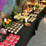 Elegancki stół cateringowy z finger food i deserami: tartaletki z owocami, panna cotta, mini kanapki i roladki – menu Deluxe.