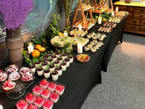 Elegancki stół cateringowy z finger food i deserami: tartaletki z owocami, panna cotta, mini kanapki i roladki – menu Deluxe.