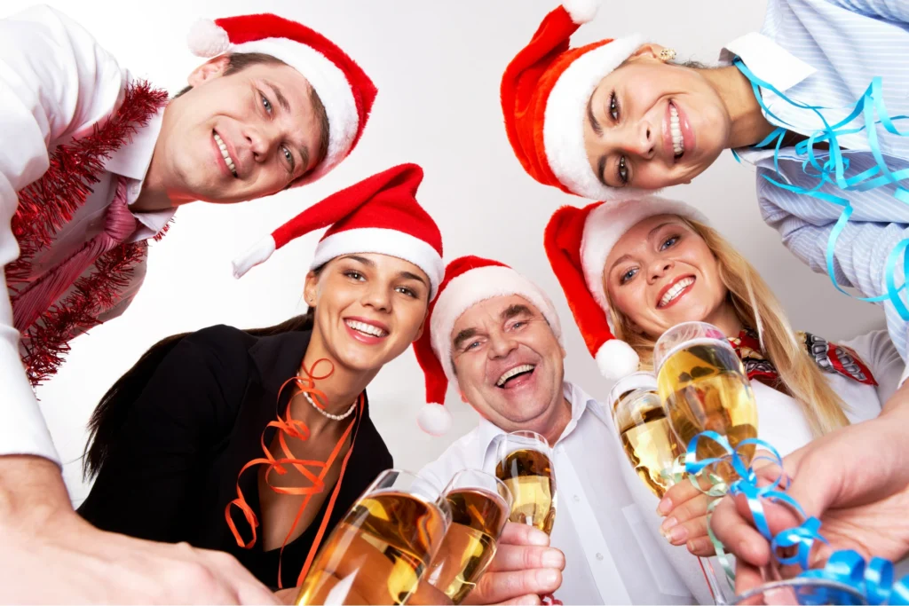 Zespół pracowników w czapkach Mikołaja świętujący firmową imprezę świąteczną z kieliszkami szampana – radosna integracja zespołu w Warszawie